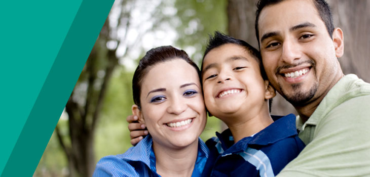 A happy young boy in a park, being hugged by his smiling parents